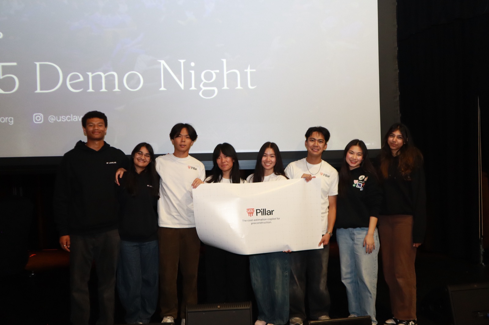 The Pillar team holding their banner on stage under the Demo Night screen.