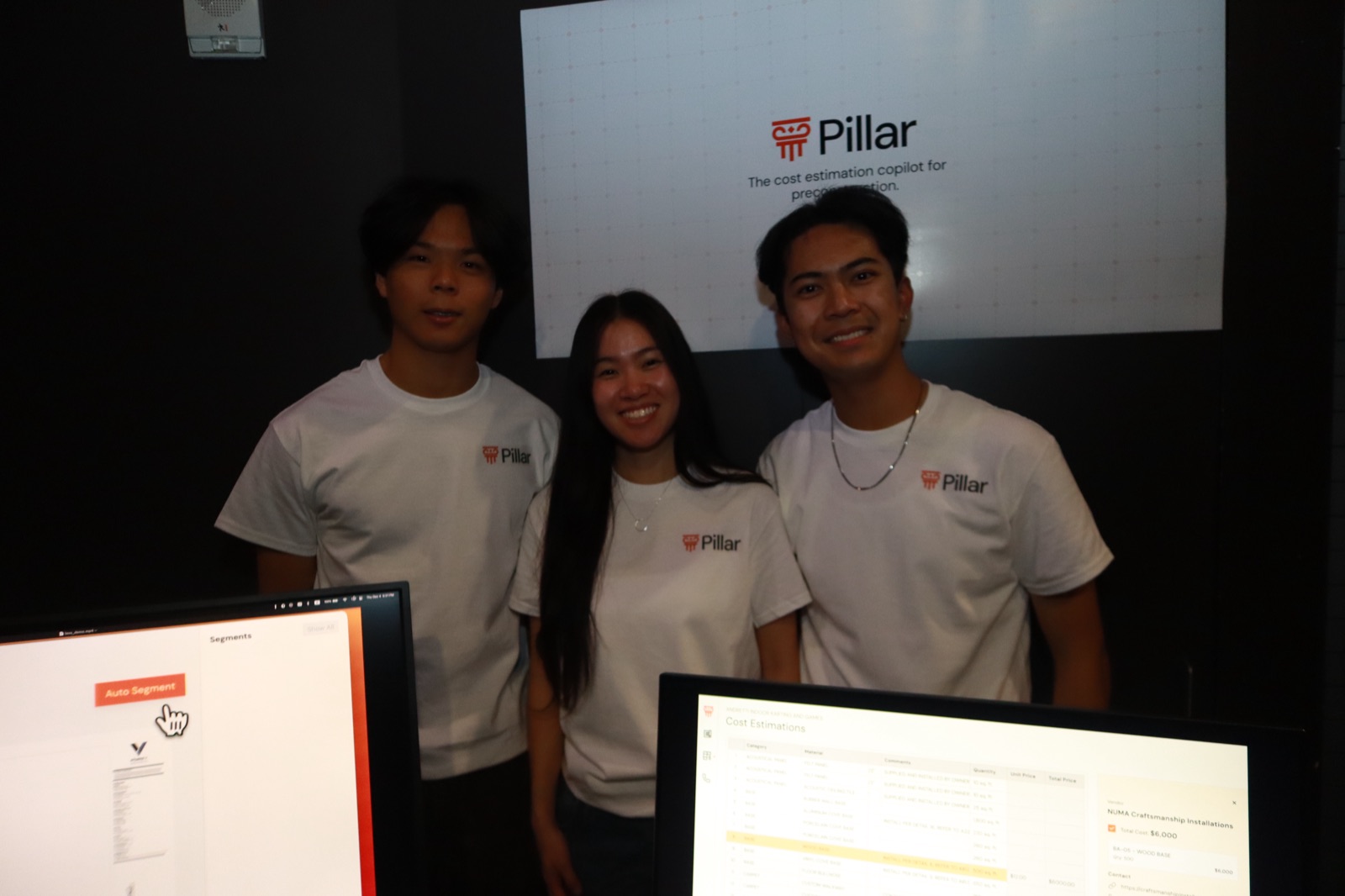 Three Pillar teammates in matching tees standing in front of the Pillar pitch screen at Demo Night.